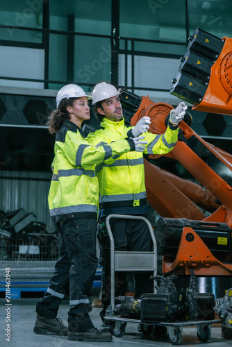 Industrial engineers team discussion robotic arm maintenance in factory warehouse. Concept of heavy industrial machinery maintenance service, equipment quality inspection, smart manufacturing supple.