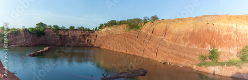 Panoramic view of a water filled quarry with steep red soil cliffs.