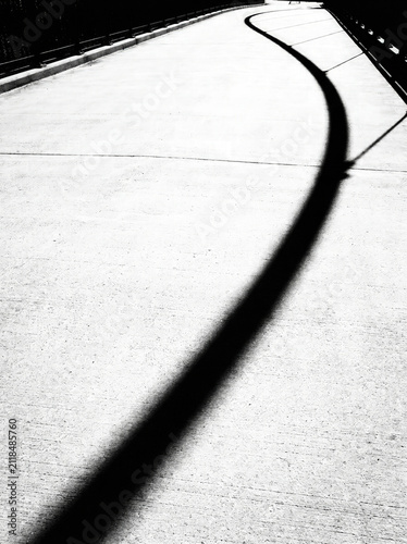 Curving black shadow crossing empty concrete bridge with railings on bright white surface, minimalist urban solitude atmosphere