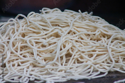 Close-up view of a large pile of fresh, raw, and uncooked white noodles prepared for cooking, showcasing the texture of traditional handmade or factory pasta