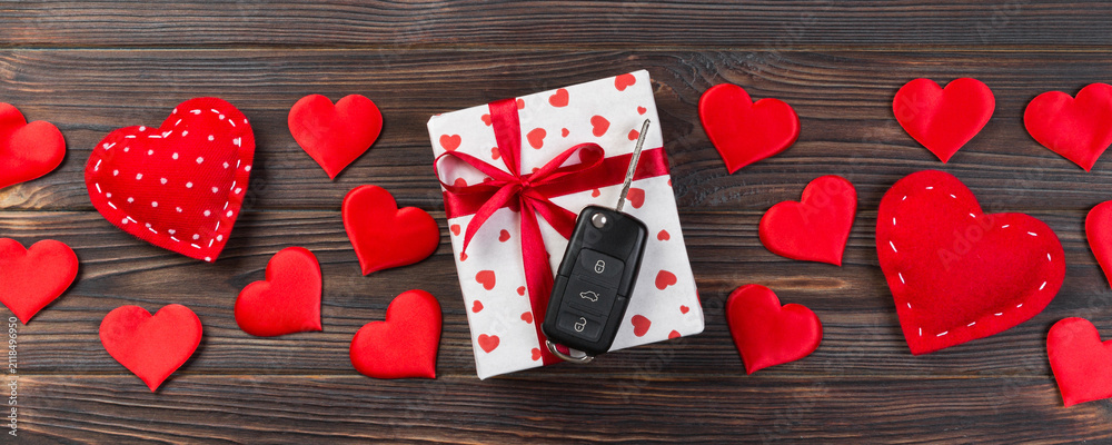 Obraz premium Valentine or other holiday handmade present in paper with red hearts, car keys and gifts box in holiday wrapper. box gift on Dark wooden table top view with copy space, empty space for design