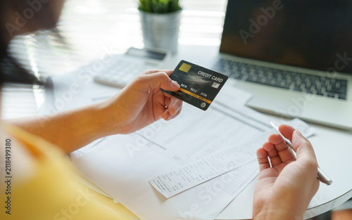 Картината върху платно Asian Woman holding a credit card while reviewing bills and budget beside a laptop, representing online payment and personal finance management