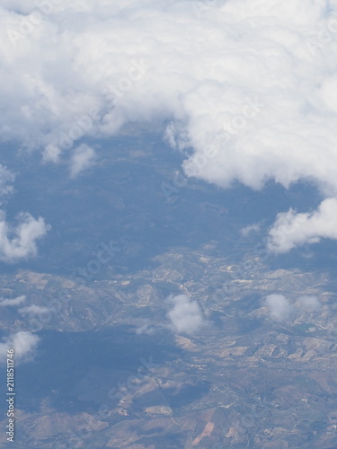 Fotografie High angle aerial view of earth surface through scattered white clouds in blue s