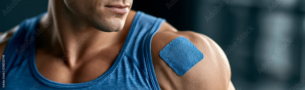 Naklejka premium Muscle Recovery: A close-up shot showcases a muscular athlete's shoulder adorned with a blue therapeutic tape, hinting at recovery and resilience after a demanding workout.