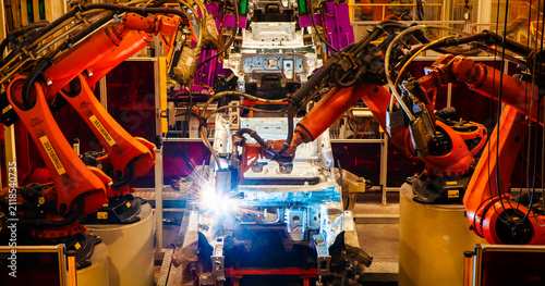Robotic arms are welding car frames on the production line at a car factory.