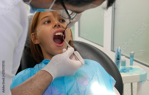 Pediatric dentist examining teeth of a brave girl sitting in dental chair