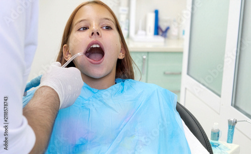 Fotografie Pediatric dentist inserting saliva ejector for young girl during treatment