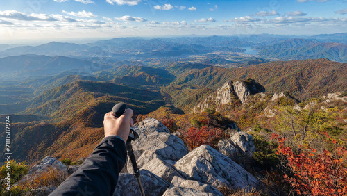 Hand holding a trekking pole above a mountain valley covered in autumn colours