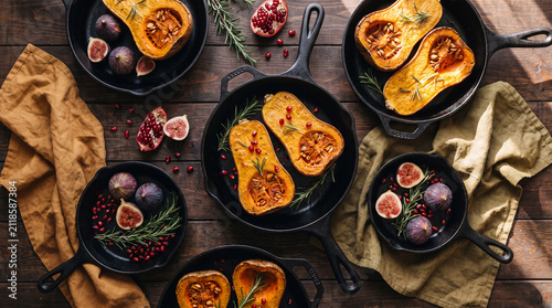 Roasted butternut squash halves with figs in cast iron skillets on a linen cloth