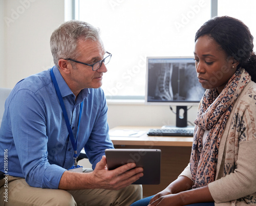 Doctor, physician or medical specialist explaining concerning examination, laboratory test, diagnosis or treatment results to patient, couple or family during serious healthcare consultation
