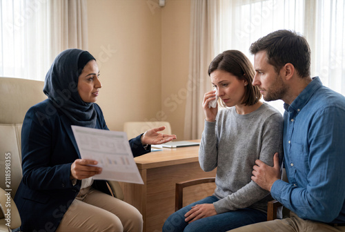 Doctor, physician or medical specialist explaining concerning examination, laboratory test, diagnosis or treatment results to patient, couple or family during serious healthcare consultation