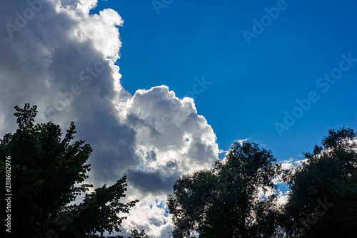 Fotografie Fluffy white clouds glowing with bright sunlight dominate a deep blue sky above