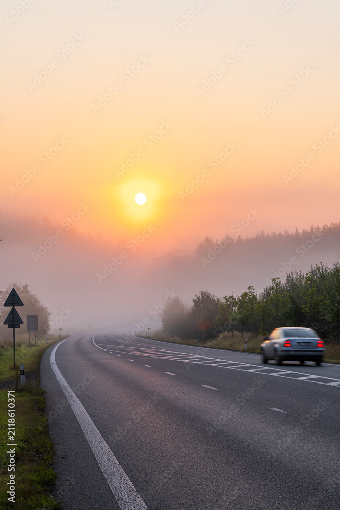 Obraz premium Car driving on foggy road at sunrise in morning