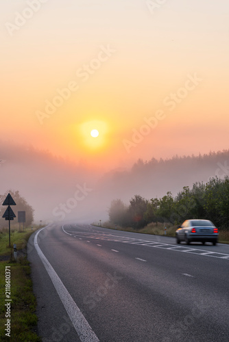 Car driving on foggy road at sunrise in morning