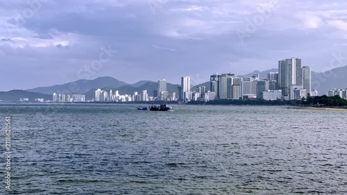 Two traditional fishing boats head out to sea at dusk with the modern skyline of Nha Trang in the background. Cloudy evening over the tropical coastline of Vietnam.