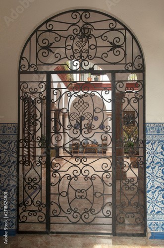 Ornate wrought iron gate opening to a traditional Andalusian patio with ceramic tiles, Spain