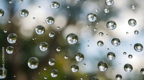 Close-up of macro water droplets on a transparent glass window pane reflecting colorful background nature scenery