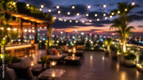 atmospheric blurred bokeh view of an upscale rooftop terrace lounge at dusk, featuring string lights, lounge seating, and a shimmering urban city skyline background.