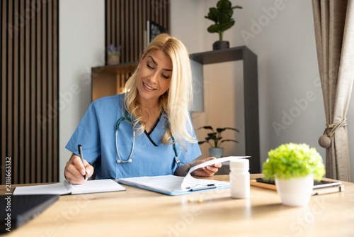 Healthcare professional wearing scrubs and stethoscope writing on a clipboard, managing patient records and prescriptions in an office