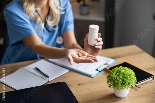Healthcare professional wearing blue scrubs holding oral tablets and a white bottle, offering treatment and prescription