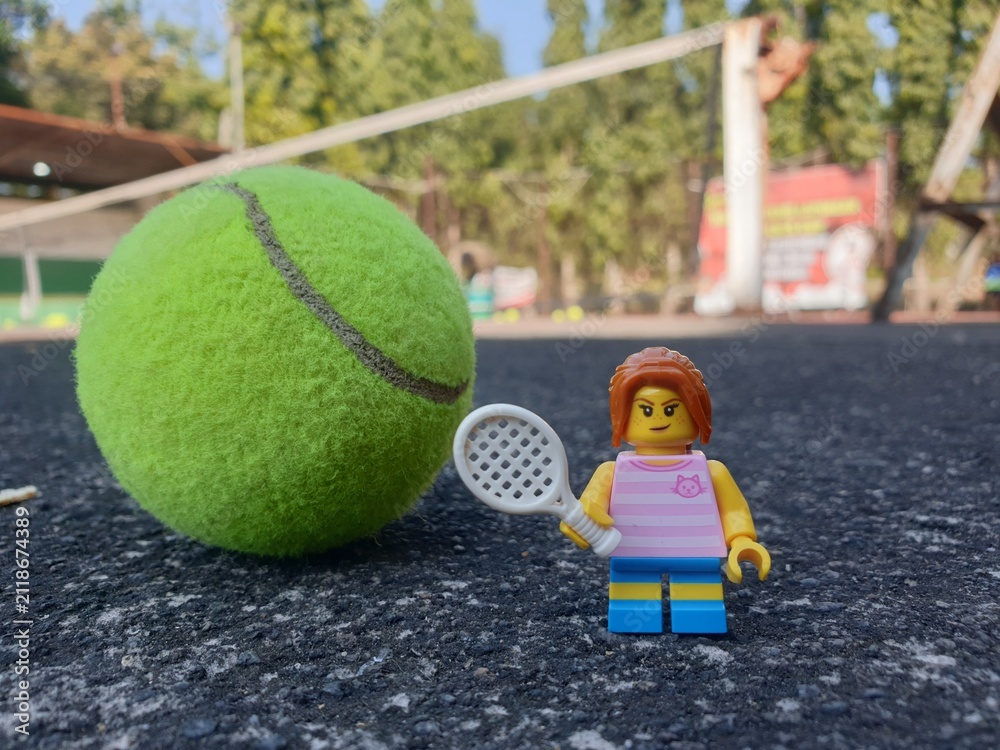 Fototapeta premium Indonesia - August 31, 2024 : Mini toy of action figure at tenniscourt with blurred background. Sport photography concept design. Miniature Young girl with tennis ball and racket.