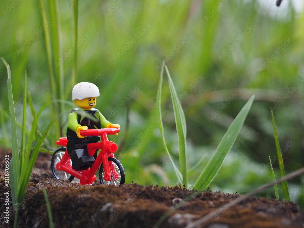 Fototapeta premium Indonesia - November 27, 2019 : Mini toy of action figure at grassland with blurred background. Toy photography concept. Bicycle at outdoor with green grass conceptual design.