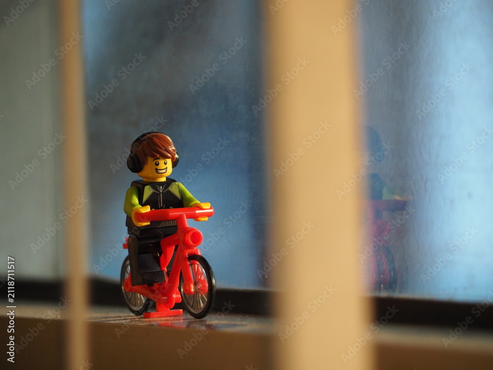 Fototapeta premium Indonesia - September 19, 2019 : Mini toy of action figure at outdoor with blurred background. Miniature photography concept design. Minifigure of young man character riding bicycle at road.