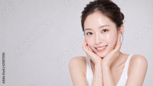透明感のあるつや肌と明るい笑顔で両手を頬に添える若い日本人女性の美容・スキンケア広告向け横長ポートレート