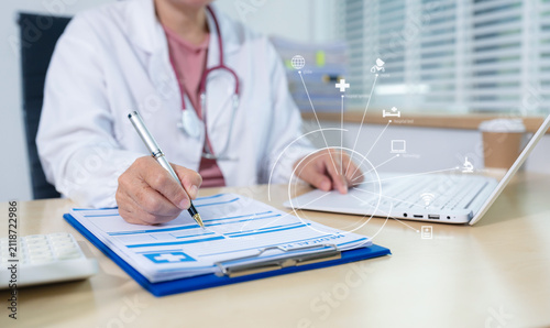 Doctor working on laptop computer and tablet and medical stethoscope on clipboard on desk, electronics medical record system EMRs concept.