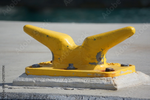 Closeup of large, yellow mooring cleat on concrete 