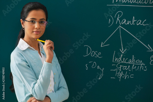 Portrait of confident young teacher against green board 