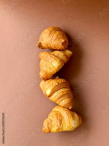 Konstfotografi Four fresh golden croissants arranged in a row on warm brown background, flat la