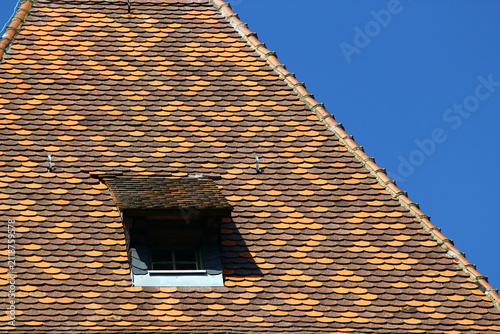 Traditional clay tile roof with patterned orange and brown shingles and small dormer window
