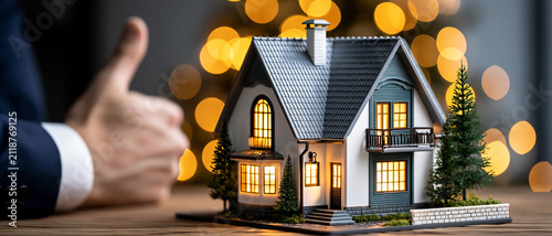 Real estate agent giving thumbs up next to a miniature model house