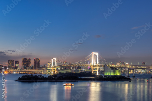Tokyo, the Odaiba waterfront development at night, reclaimed land with a large bridge and modern buildings and a Statue of Liberty replica.