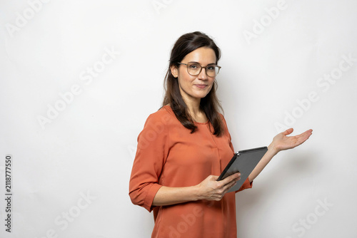 Businesswoman holding digital tablet and presenting with open hand, professional woman in orange blouse and eyeglasses isolated on white background