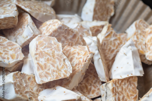 Sliced raw organic tempeh block on a clean white plate. Close up view showing the rich texture of fermented soybeans bound together by white mycelium. A healthy, plant-based vegan protein