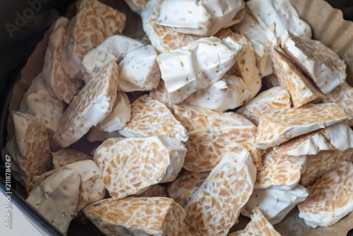 Sliced raw organic tempeh block on a clean white plate. Close up view showing the rich texture of fermented soybeans bound together by white mycelium. A healthy, plant-based vegan protein