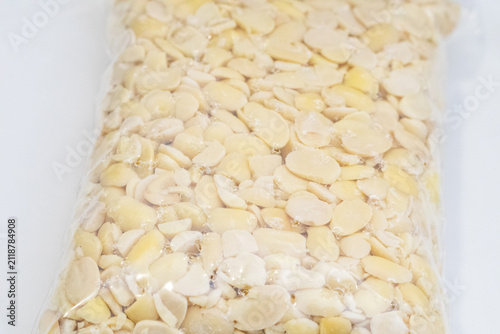 Peeled split soybeans packed tightly in a clear plastic zipper pouch, presented on a plain white surface. Highlighting raw plant based ingredients, prep work