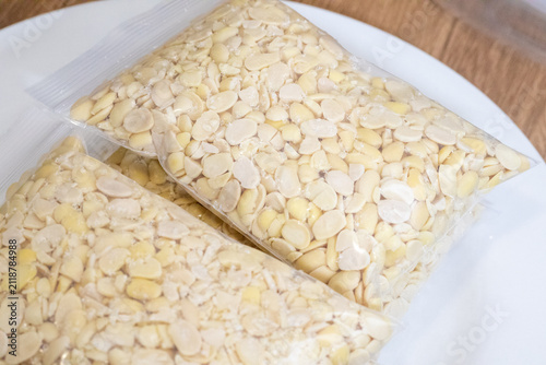 Peeled split soybeans packed tightly in a clear plastic zipper pouch, presented on a plain white surface. Highlighting raw plant based ingredients, prep work