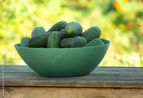 фотографія Fresh green cucumbers in a bowl on a weathered rustic wooden table against a bright blurred garden background