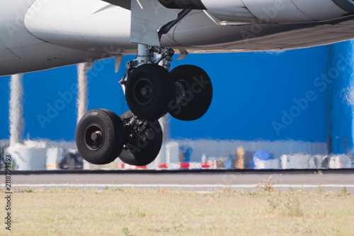 Airplane landing gear extended during an approach to an airport runway with a blue building structure behind