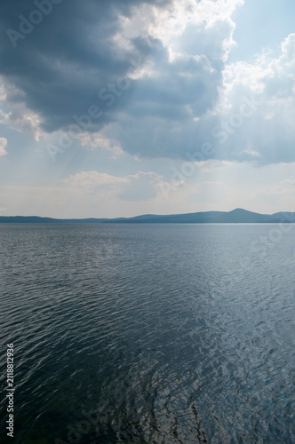 Summer view of lake Turgoyak with sunrays bursting through the cloudy sky, South Ural, Russian Federation