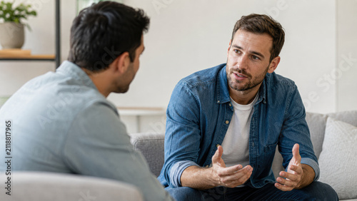 Two men engaged in a serious conversation while sitting on a couch in a cozy, modern living room.