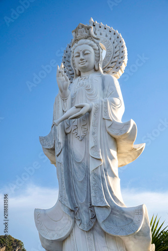 Bild auf Leinwand Low angle closeup of white marble Guanyin statue with radiant halo and raised fingers against blue sky