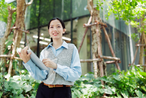Smiling businesswoman holding a tablet and stylus in a green modern office garden, representing digital work, sustainability, leadership, productivity, career growth, and professional success.
