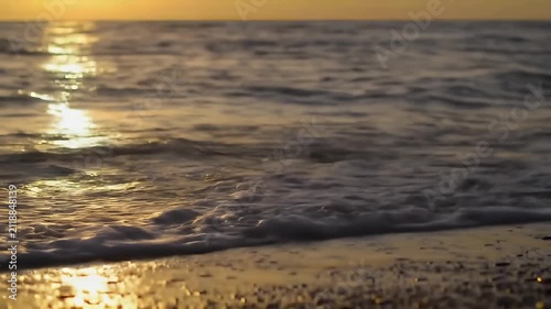 A serene golden sunset over a tranquil sea meeting a pebble-strewn shoreline at dusk