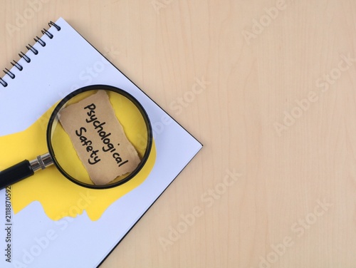 Psychological safety concept handwritten with human head paper silhouette and magnifying glass on book. Perfect for corporate culture, mental health at work, and human resource management concepts