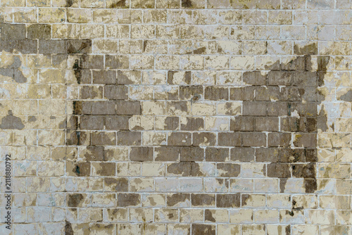 Brick wall texture with large damaged plaster patches. Weathered masonry background with exposed dark inner blocks.