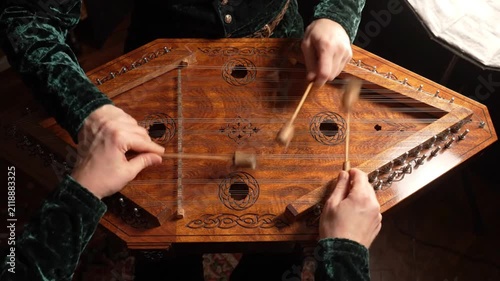 Musician playing hammered dulcimer with mallets, close-up of hands and strings.